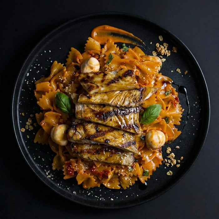 Plated dish of pasta with grilled fish and vegetables on a dark background