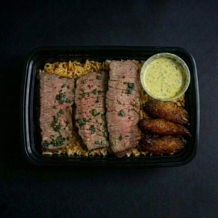 Plated meal with sliced meat, rice, and a side of sauce on a dark background