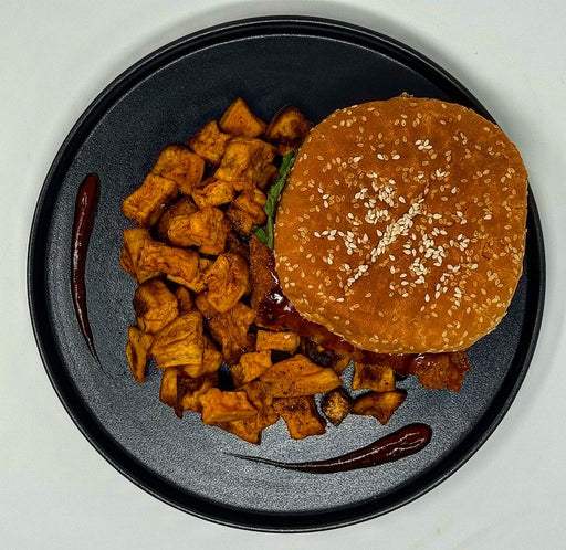 Burger with sesame seed bun and side of fried potatoes on a black plate.