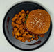 Burger with sesame seed bun and side of fried potatoes on a black plate.
