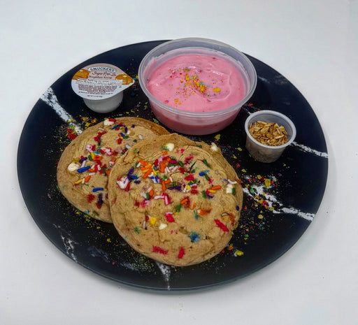 Cookies with colorful sprinkles on a black plate with pink icing and nuts. A breakfast meal made by spartan meal preps.