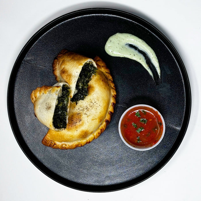Pastry with spinach filling on a black plate with dipping sauces