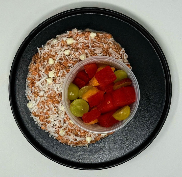 Coconut-covered treat with a container of fruit on a black plate