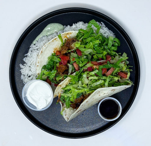 Tacos with lettuce, tomatoes, and rice on a black plate with side dishes.