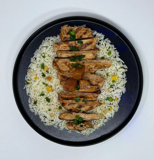 Plated dish of rice with grilled chicken and garnishes on a white background