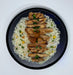 Plated dish of rice with grilled chicken and garnishes on a white background