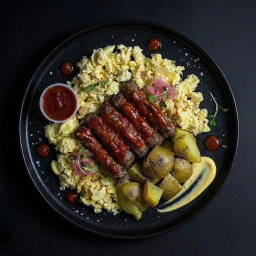 Plated dish with scrambled eggs, sausages, and potatoes on a dark background