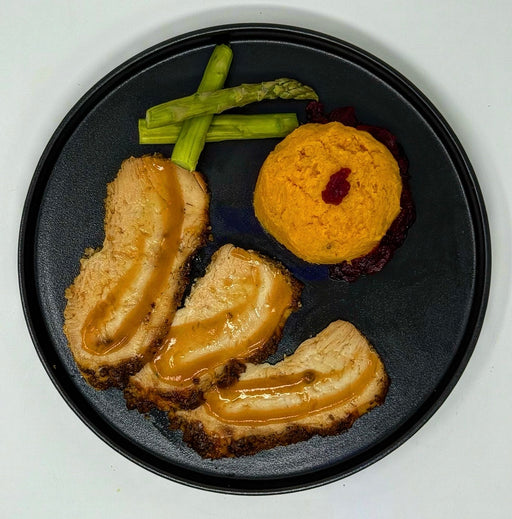 Plated dish with roasted meat, mashed potato, and asparagus on a black plate.