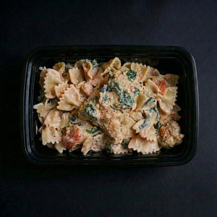 Pasta dish with spinach and tomatoes in a black container on a dark background