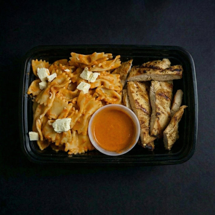 Plated dish with pasta, grilled chicken, and a side of sauce on a dark background