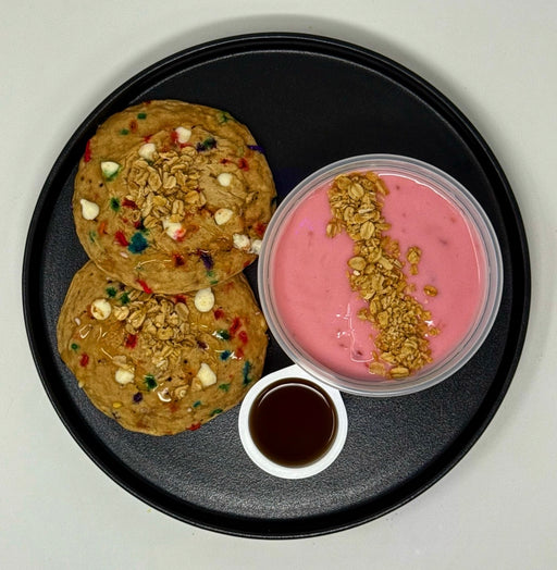 Two cookies and a container of pink yogurt with granola on a black plate.