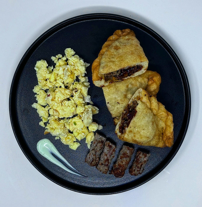 Plate of food with three empanadas, eggs, and on a dark plate. pieces of turkey sausage on a black plate. Healthy meal made by spartan mela preps new jersey.
