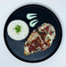 Plated dish of chicken with tomato sauce over white rice on a dark plate.