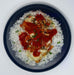 Plated dish of chicken with tomato sauce over white rice on a dark plate.