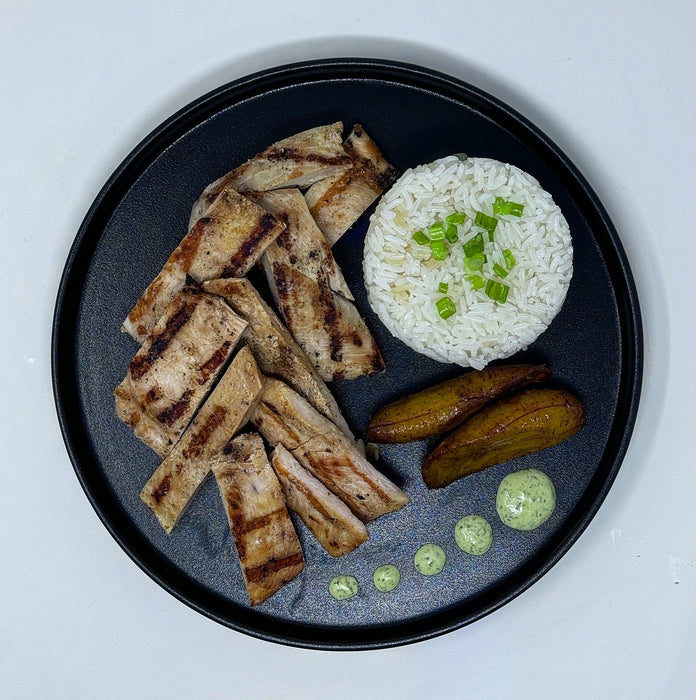 Plated dish with grilled meat, rice, and vegetables on a white background