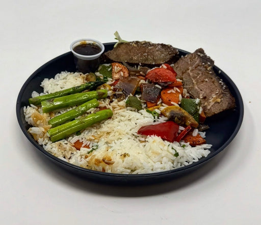 A plate of Korean Teriyaki steak bowl with jasmine rice, mixed vegetables, and steak, served with a side sauce.
