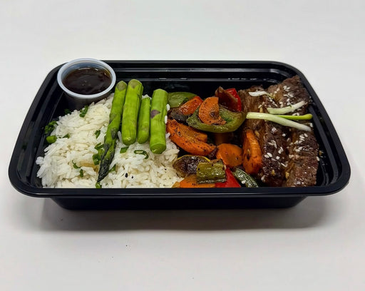 A plate of Korean Teriyaki steak bowl with jasmine rice, mixed vegetables, and steak, served with a side sauce on a black plate meal made by spartan meal preps nj.