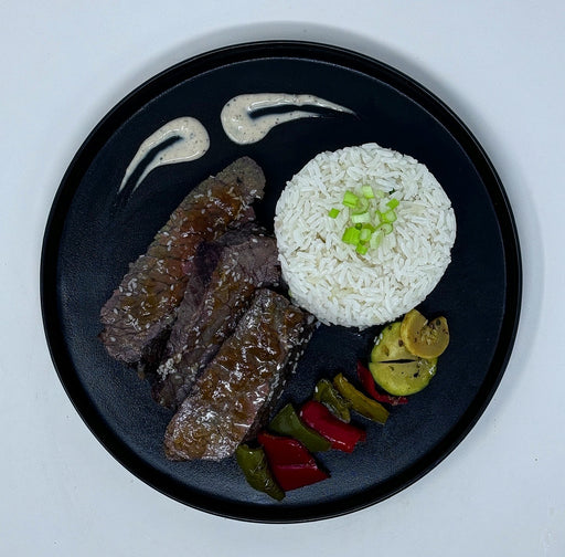Steak with rice and vegetables on a black plate