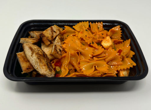 A plate of Spartan Chicken Pasta which includes grilled chicken and farfalle pasta with tomato sauce and vegetables on a black plate.