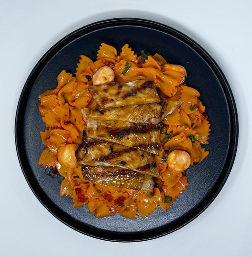 A plate of Spartan Chicken Pasta which includes grilled chicken and farfalle pasta with tomato sauce and vegetables.