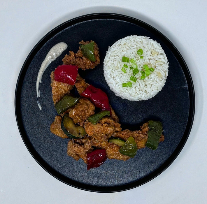 Plated dish with fried chicken, peppers, and rice on a dark plate.