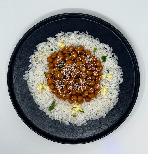 Black plate with white rice and a circular arrangement of brown chickpea dish on a white background