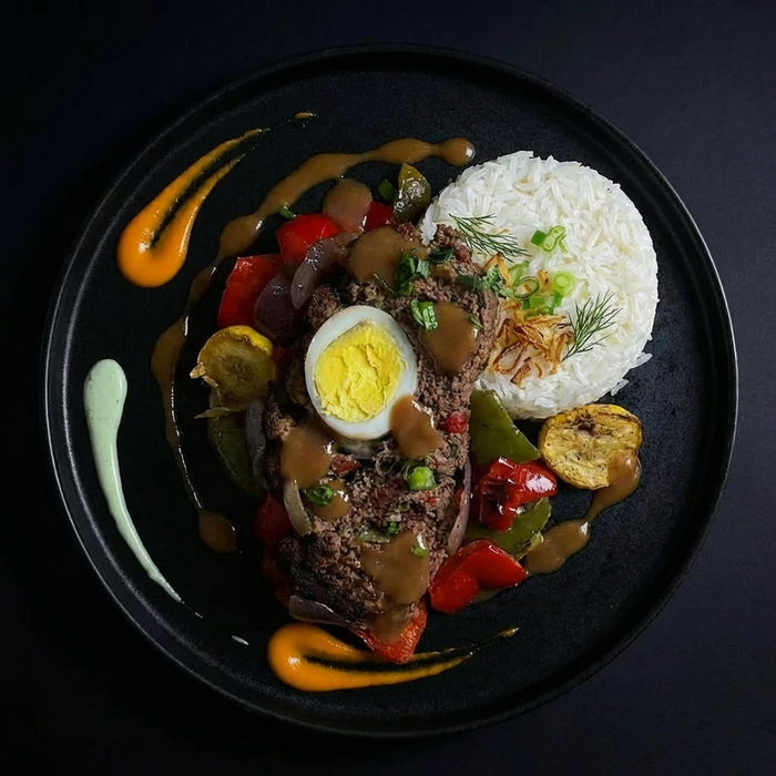 Plated dish with meatloaf, boiled egg, vegetables, and rice on a dark background