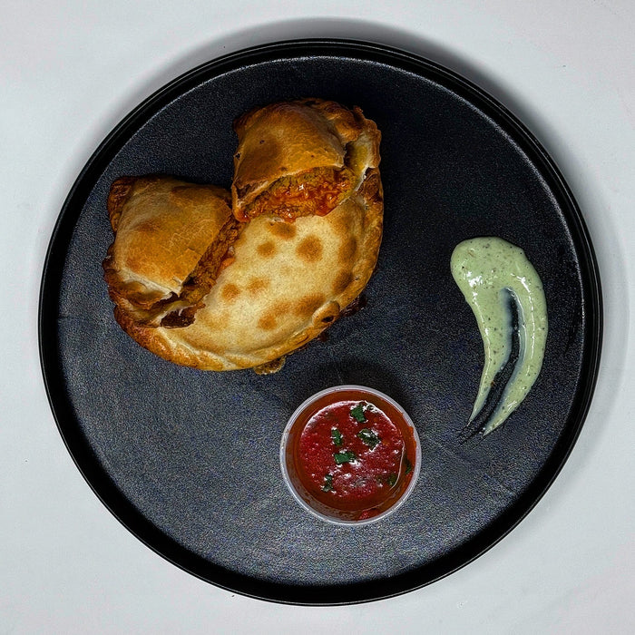 two teriyaki stuffed empanadas on a black plate with a house sauce. Healthy meal made by spartan meal preps a new jersey meal delivery company. 