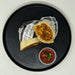 Burrito on a black plate with salsa on a white background